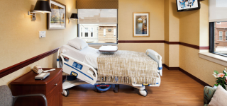 Hospice room with a bed facing the window, TV, lamps and a blanket