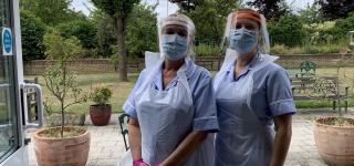Two nurses in full PPE outside a building