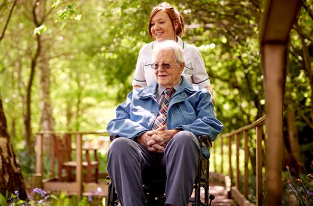 A hospice nurse with a patient in a wheelchair admiring the hospice gardens