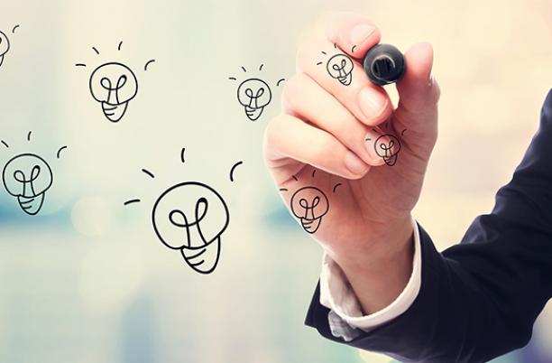 Stock photo of a hand, holding a pen, drawing lightbulbs on a transparent surface
