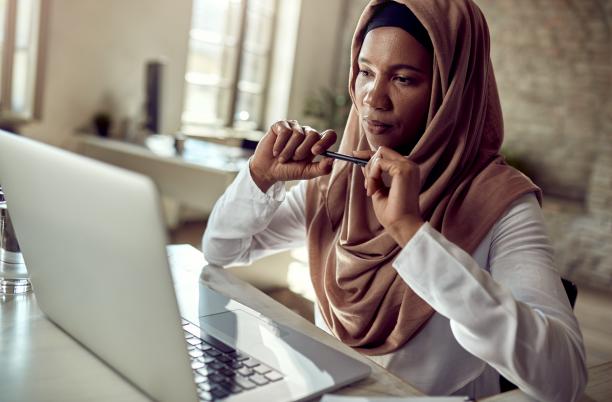 Woman wearing head scarf sitting at desk with laptop