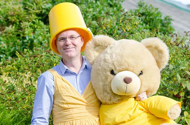 Going yellow at Wirral Hospice, a man with a yellow bucked on his head holding a yellow bear