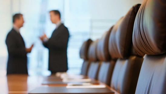Stock photo of two people talking in the distance, in a boardroom with a table and chairs