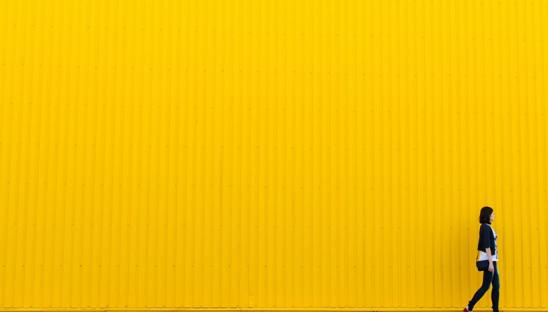 A stock image of a woman walking past a yellow background